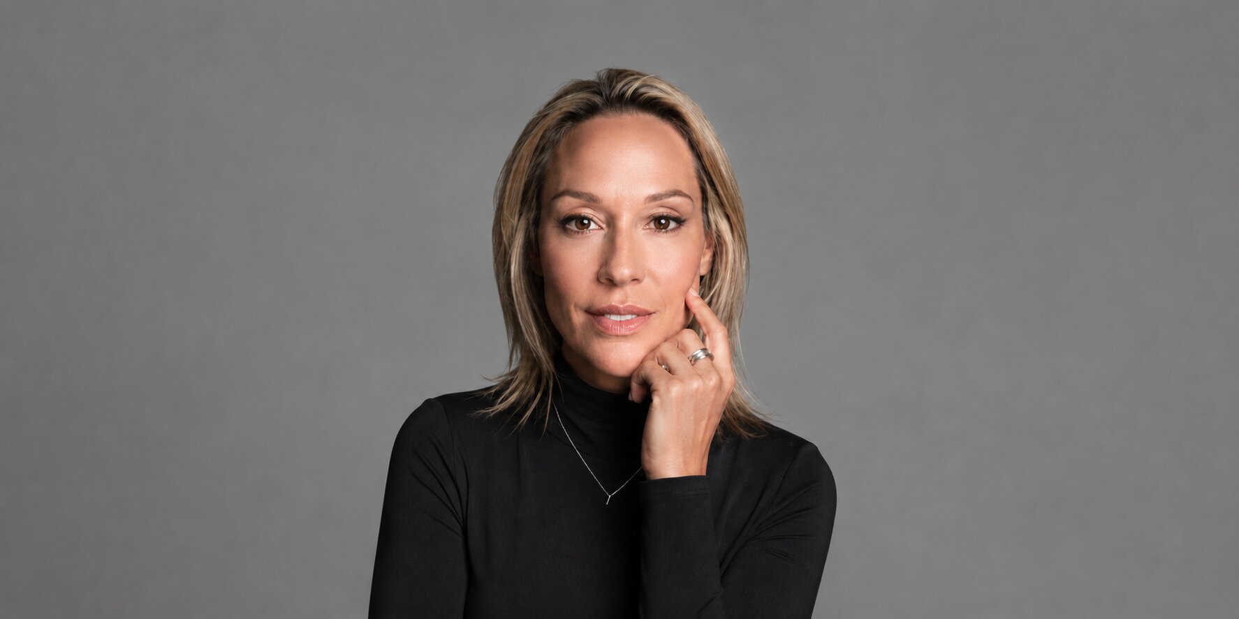 Coach Julianne wearing a black turtleneck in a professional studio portrait against a gray background.