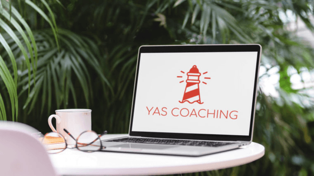 Laptop on outdoor table displaying YAS Coaching lighthouse logo beside coffee cup and glasses, symbolizing Yasmina Rauber’s leadership coaching work.