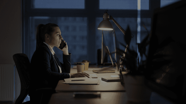 Business professional working late at a desk while talking on the phone in an office.
