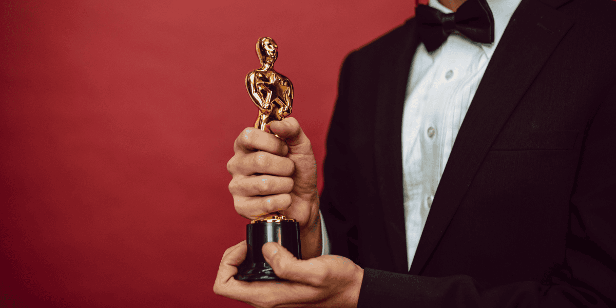 Person in a tuxedo holding a gold award statuette against a red background.